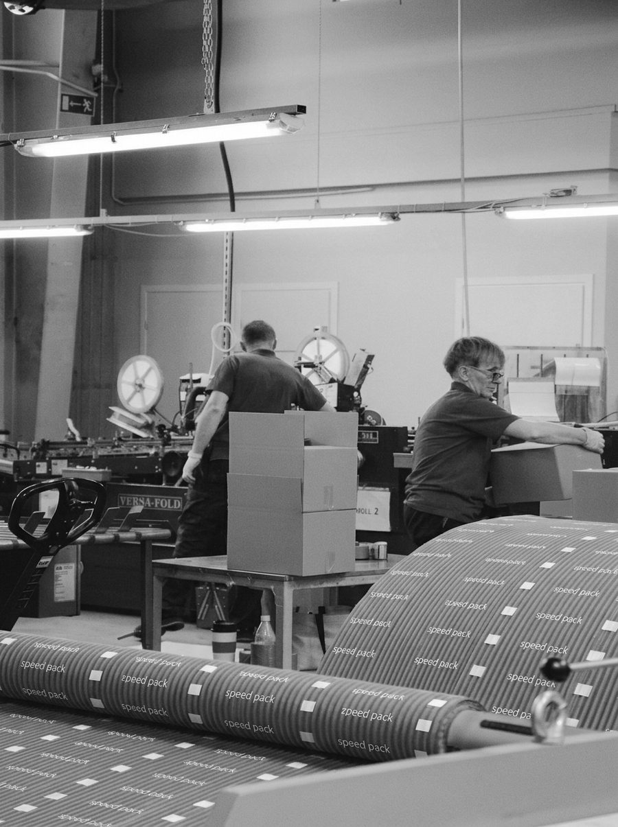 Two operators at a folder-gluer with assembled cartons stacked between them